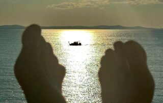Füsse im Vordergrund beim Entspannen am Meer, im Hintergrund Boot im Sonnenlicht – Symbol für Loslassen und innere Ruhe.